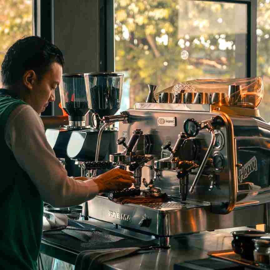 Barista using the Faema E61 Legend espresso machine with dual handles in a modern café – Dual Handle in Action at Café. The Faema E61 Legend in professional use—dual group head model delivering precision espresso shots with timeless flair.