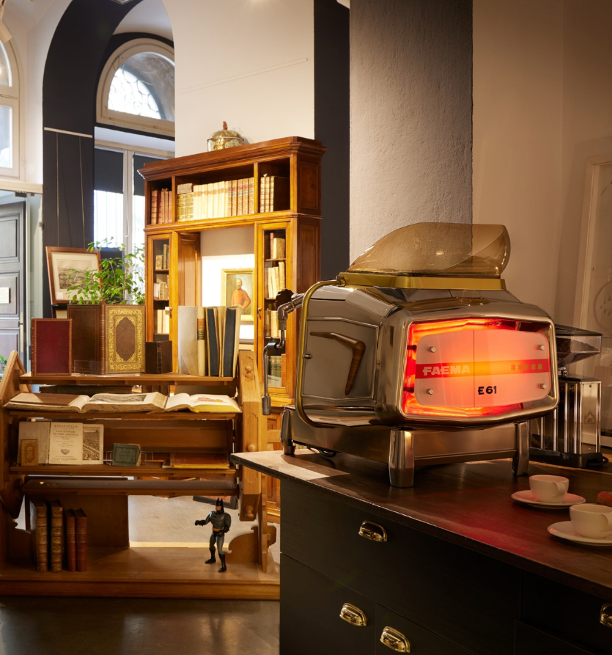 Faema E61 Legend Espresso Machine in a vintage library cafe setting, glowing red back panel – Classic Espresso Machine in Timeless Library Ambience
The Faema E61 Legend glowing in a vintage library café – where classic design meets classic taste.