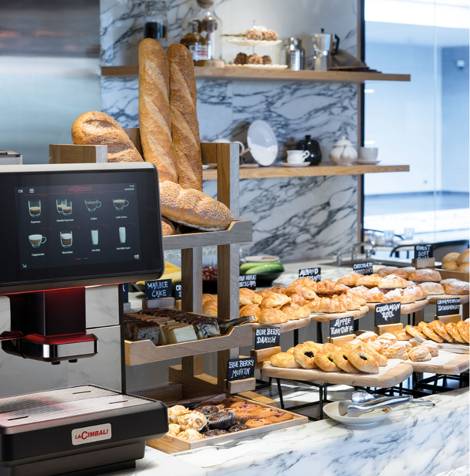 La Cimbali S-Lite Automatic Espresso Machine in modern bakery café with fresh pastries and touchscreen menu - S-Lite Automatic Espresso Machine – Perfect for Café & Bakery Environments | La Cimbali - Elevate your café’s service with the La Cimbali S-Lite—sleek touchscreen design, fast brewing, and ideal for bakeries and coffee shops.