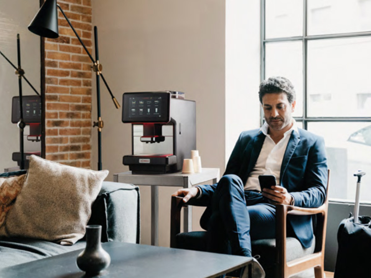 S-Lite Automatic Espresso Machine in a sophisticated business lounge with a suited man enjoying coffee - S-Lite Espresso Machine for Business Lounges & Hospitality - Create a refined hospitality experience with the S-Lite—perfect for executive lounges and lobbies.